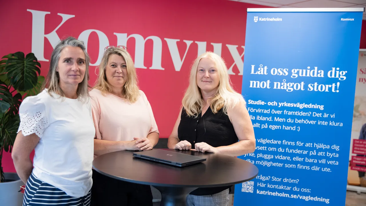Tre glada kvinnor framför en rosa vägg med texten Komvux.