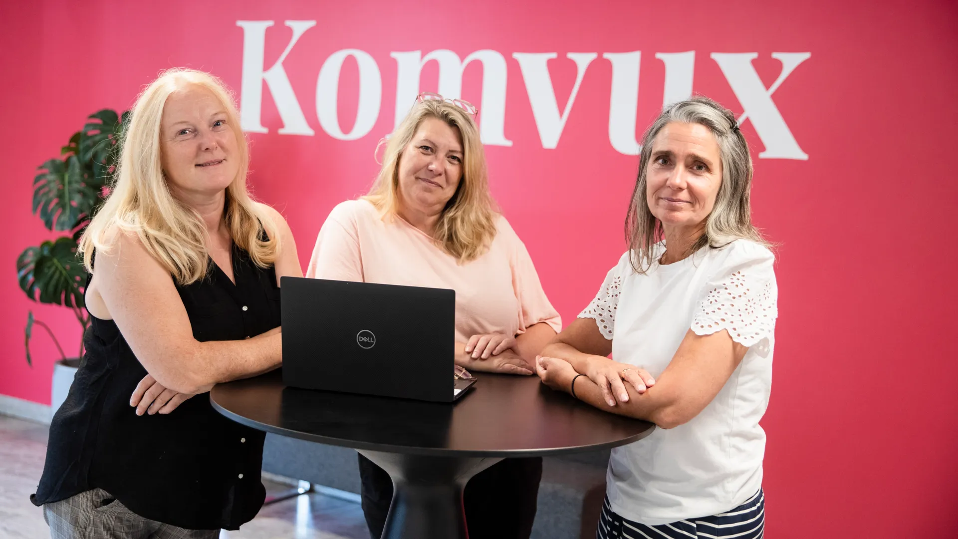 Tre glada kvinnor framför en rosa vägg med texten Komvux.