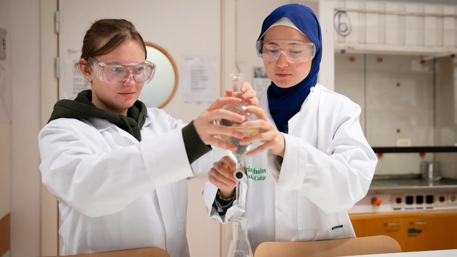 Elever i labkläder gör experiment i en kemisal.