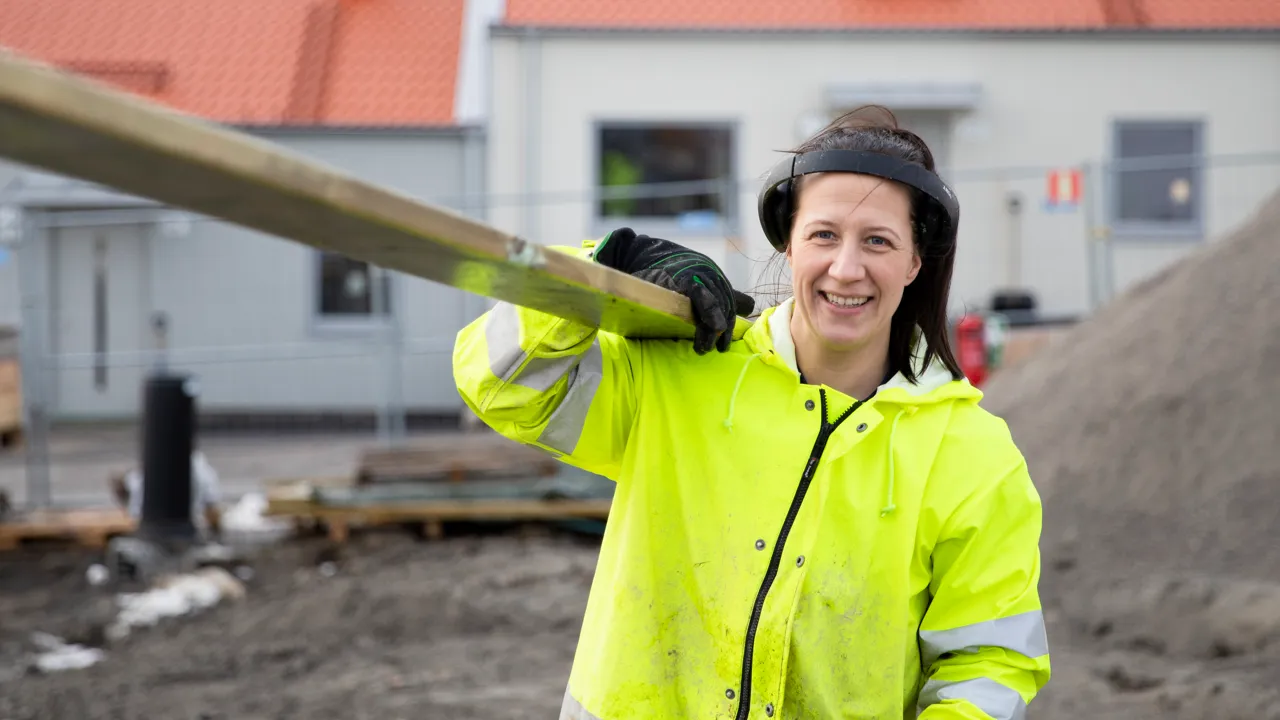 En kvinna i en gul jacka som håller i en lång planka.